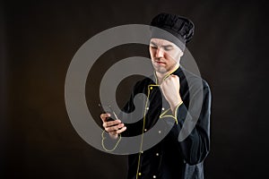 Young male dressed in a black chef suit reading and sending text messages on cellphone looking nervously