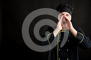 Young male dressed in a black chef suit shouting with her hands to her mouth