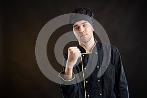 Young male dressed in a black chef suit showing fist