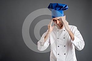 Young male dressed in a white chef suit has headache