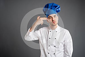 Young male dressed in a white chef suit showing shot head gesture