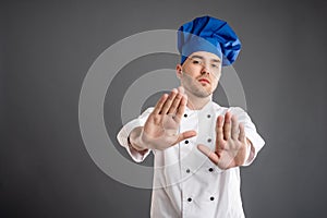 Young male dressed in a white chef suit showing stop sign with boath hands
