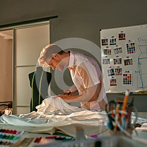 Young male dressmaker cutting cloth with scissors