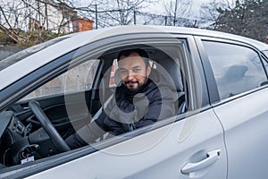 A young male driver looks at camera and smiles while sitting on car seat before driving