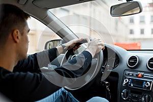 Young male driver sitting in the car and holding the wheel.