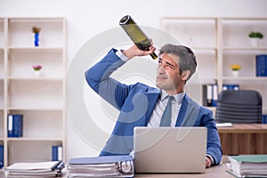 Young male employee drinking alcohol at workplace