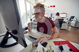 A young male employee is drinking a coffee while working in the office. Employees, job, office