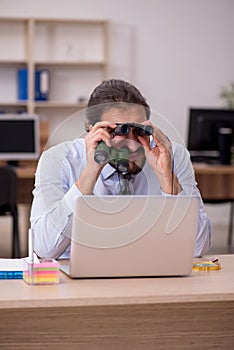 Young male employee holding binoculars in industrial espionage c