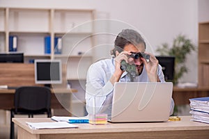 Young male employee holding binoculars in industrial espionage c