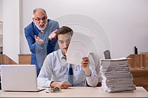 Young male employee and old boss burning papers at workplace