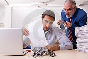 Young male employee and old boss burning papers at workplace