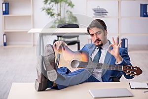 Young male employee playing guitar at workplace