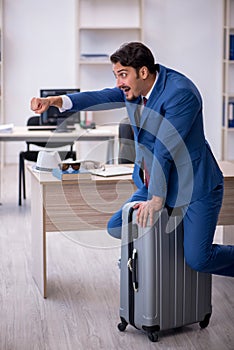 Young male employee preparing for trip at workplace