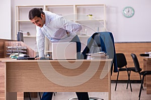 Young male employee suffering from backpain at workplace