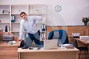 Young male employee suffering from backpain at workplace