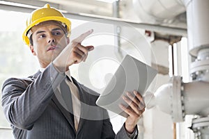 Young male engineer with digital tablet pointing away in industry