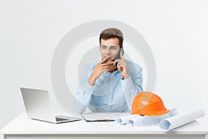 Young male engineer speaking on the phone in his office on grey