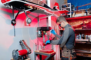 Young male engineer or technician using drill for drone details in lab. Aircraft capable of GPS surveillance. Carbon.