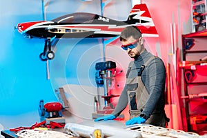 Young male engineer or technician working on drone details in lab. Aircraft capable of GPS surveillance. Carbon.