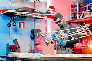 Young male engineer or technician working on drone details in lab. Aircraft capable of GPS surveillance. Carbon.