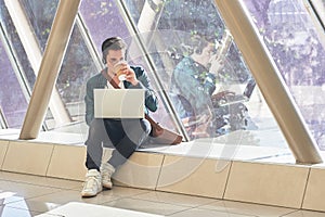 young male entrepeneur student waiting working on laptop in sunny corridor photo