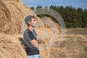 Young male farmer in grey t-shirt standing at haystack looking to the side, copy space