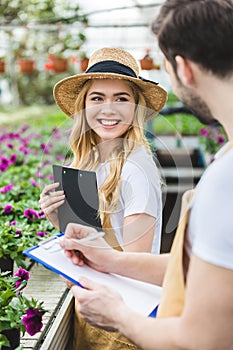 Young male and female gardeners holding clipboards by flowers photo