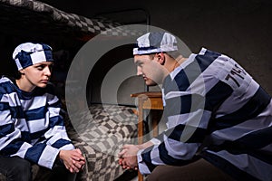 Young male and female prisoners wearing prison uniform sitting a photo