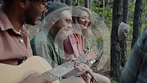 Young male and female tourists singing songs to guitar enjoying weekend in autumn forest