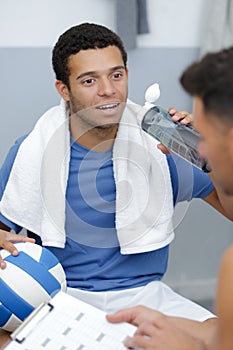 Young male footballer with coach drinking water