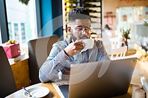 Young male freelancer chatting on mobile phone while sitting front open laptop computer in natural food cafe. Handsome man reading