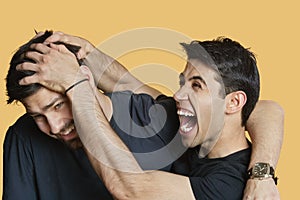 Young male friends playfighting over colored background