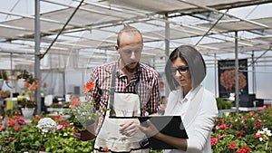 A young male gardener demonstrates the products of the flower shop to a girl sales manager.