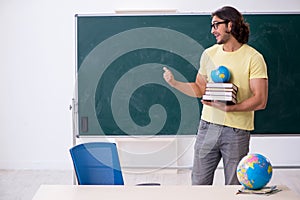 Young male geography teacher in front of blackboard