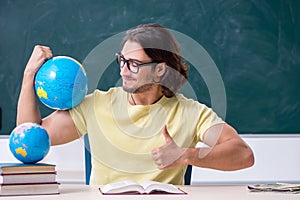 Young male geography teacher in front of blackboard