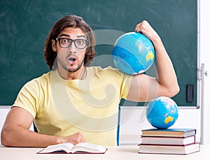 Young male geography teacher in front of blackboard