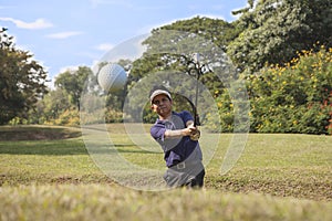 Young male golf player grey pants chipping golf ball out of a sa