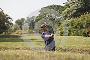 Young male golf player grey pants chipping golf ball out of a sa