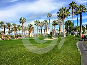 A young male golfer walking towards the green on a par 4 surrounded by water and palm trees in the background on the desert oasis