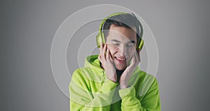 Young male in green sweatshirt listening to music. Man wearing green headphone enjoying his music at gray background