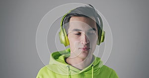 Young male in green sweatshirt listening to music. Man wearing green headphone enjoying his music at gray background