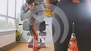 Young male in grey sportswear exercising abdominals in the gym - girl looking to him