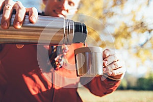 Young male hands pouring a hot tea into cup . from thermos flask in autumn forest close up image