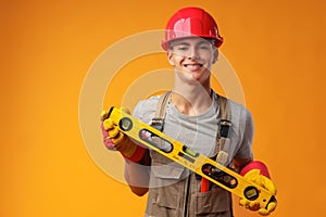 Young male handyman holding construction spirit level on yellow background
