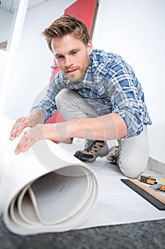 Young male handyman rolling carpet on floor at home