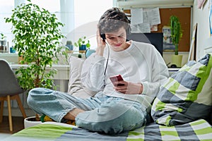 Young male in headphones looking in smartphone while sitting on couch at home