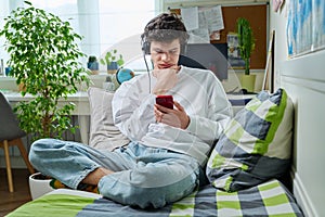 Young male in headphones looking in smartphone while sitting on couch at home