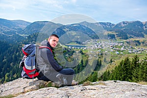 Mladý mužský turista s batohom relaxuje na vrchole hory počas pokojného letného dňa.