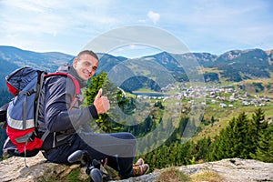 Young male hiker with backpack relaxing on top of a mountain during calm summer day.