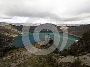 Young male hiker in blue jacket at andean volcano caldera crater lake Quilotoa rim ridge loop Cotopaxi Ecuador andes photo